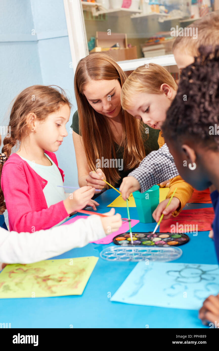 Pittura per bambini nella classe di pittura con acquarello e spazzola sotto la supervisione di un insegnante di scuola materna Foto Stock