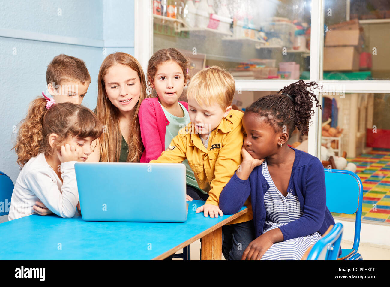 Un gruppo di bambini e insegnanti insieme al computer portatile in età prescolare o asilo nido Foto Stock