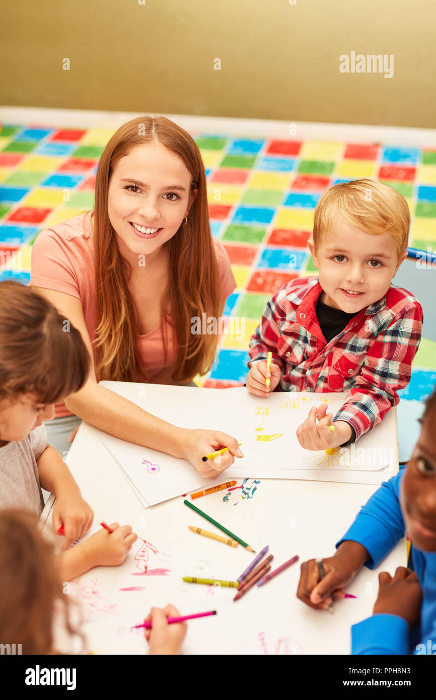 Una donna come educatore dipinge e disegna insieme con i bambini in una scuola materna o asilo nido Foto Stock