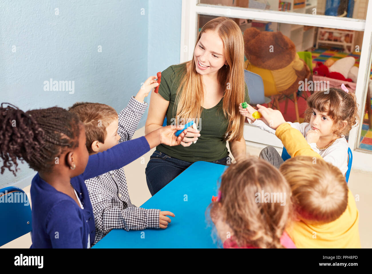 Insegnante di scuola materna e il gruppo di bambini con gioco l'impasto in un laboratorio artigianale in kindergarten Foto Stock
