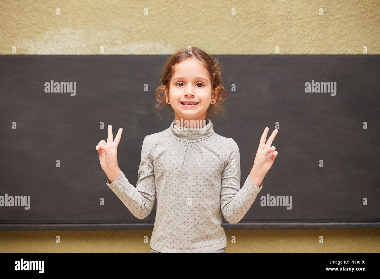 Bambina come un allievo nella posa di vittoria dopo un esame di fronte a una lavagna nella scuola elementare Foto Stock