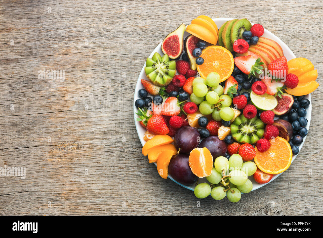 Una sana frutta, fragole lamponi arance Prugne Mele Kiwi uve mirtilli sul grigio scuro tavolo in legno, vista dall'alto, copia spazio per Foto Stock