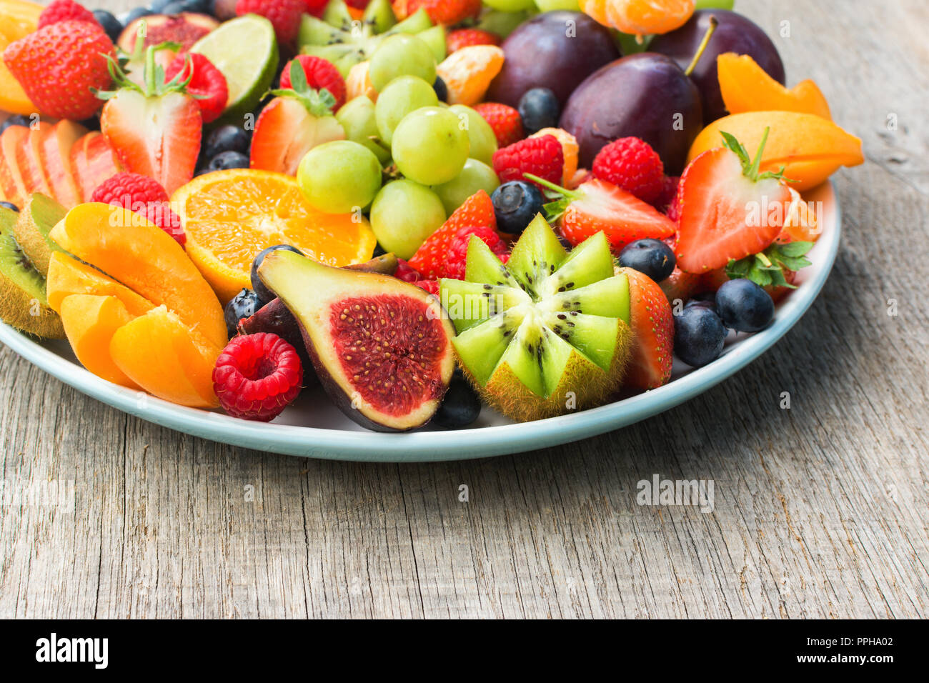 Una sana frutta e bacche platter, Fragole Lamponi arance Prugne Mele Kiwi uve mirtilli sul grigio scuro tavolo in legno, close up, cop Foto Stock