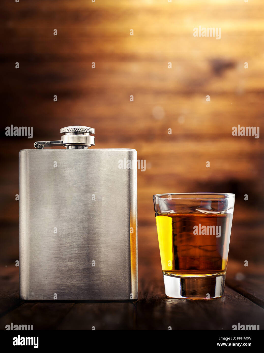 Il whiskey di metallo fiaschetta closeup, su di un tavolo di legno con un colpo di vetro riempito con alcol di whisky Foto Stock