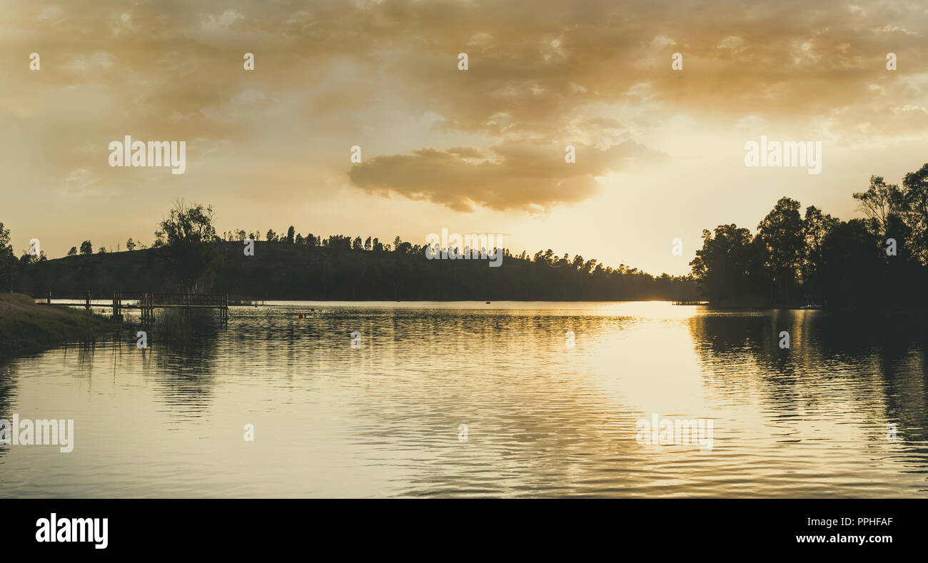 Tramonto sul lago con la luce del sole illuminando le nuvole e riflessi nell'acqua Foto Stock