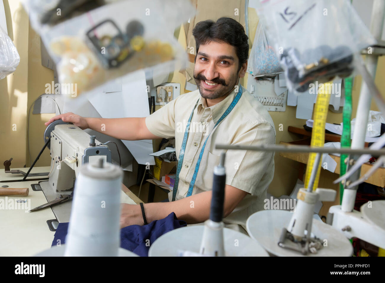 Felice cercando di adattare a lavorare sulla macchina per cucire nella sua bottega con accessori di sartoria appeso attorno a. Foto Stock