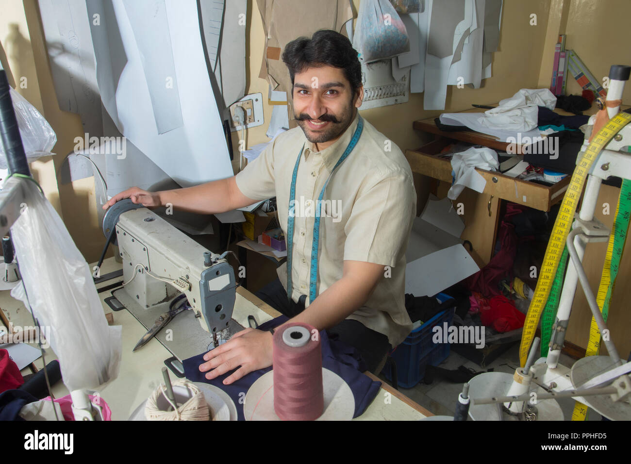 Felice cercando di adattare a lavorare sulla macchina di cucitura Cucitura di un tessuto nella sua piccola officina. Foto Stock