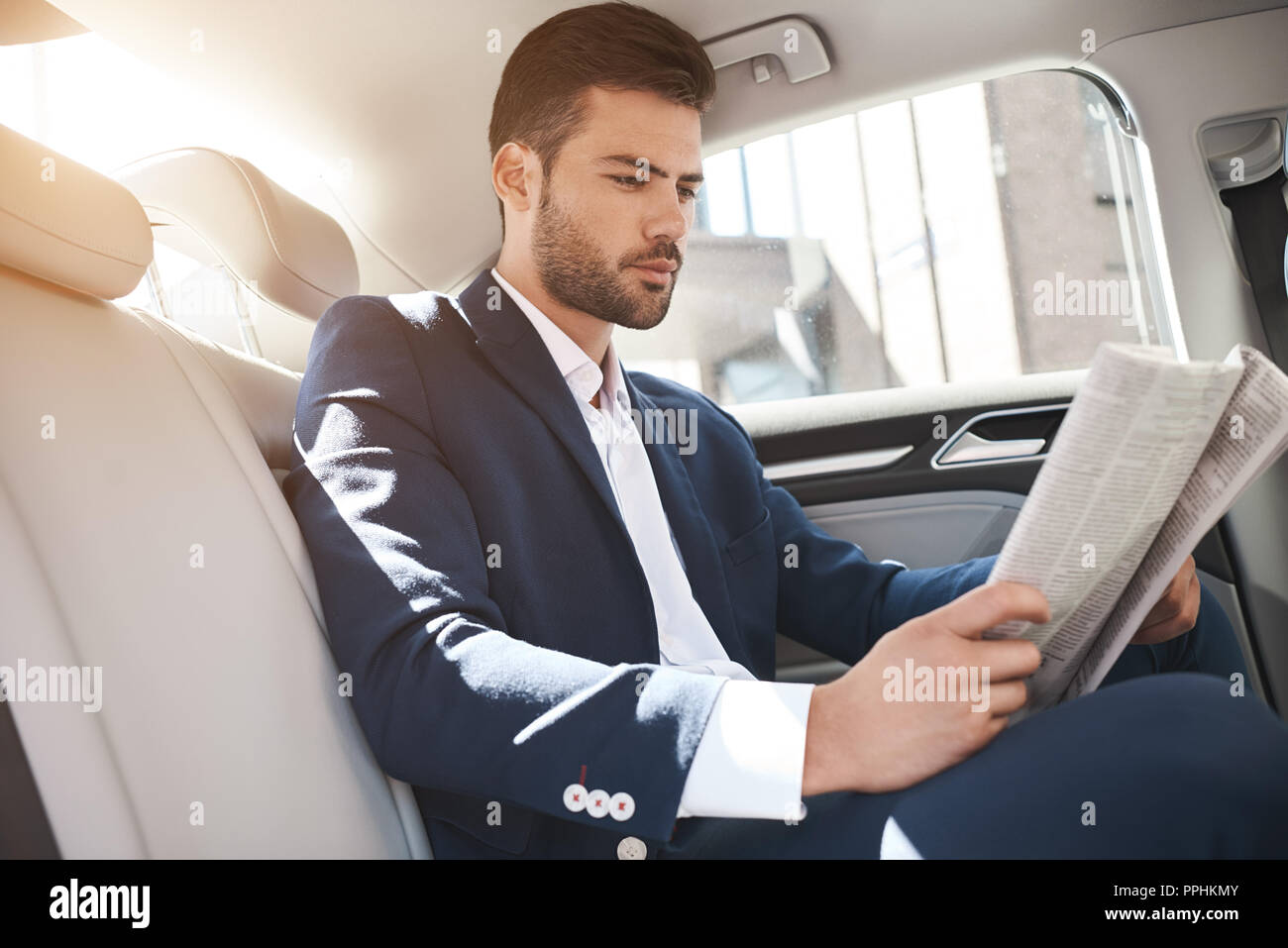 Giovane imprenditore elegante legge giornale sul sedile posteriore della macchina Foto Stock