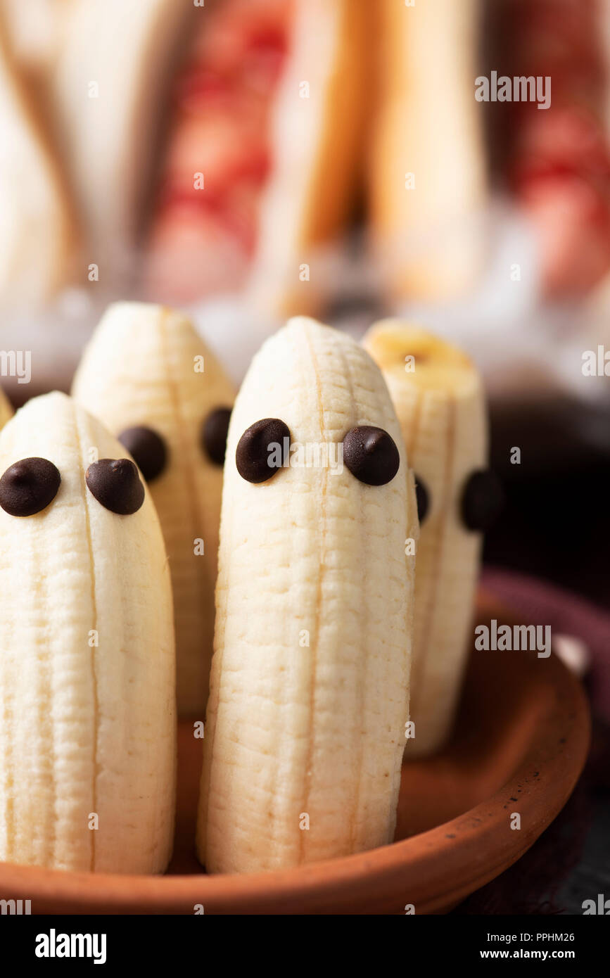 Primo piano di alcune divertenti halloween alimentari quali le banane con gli occhi come fantasmi o hotdog in forma di sanguinosa delle dita su un tavolo rustico Foto Stock