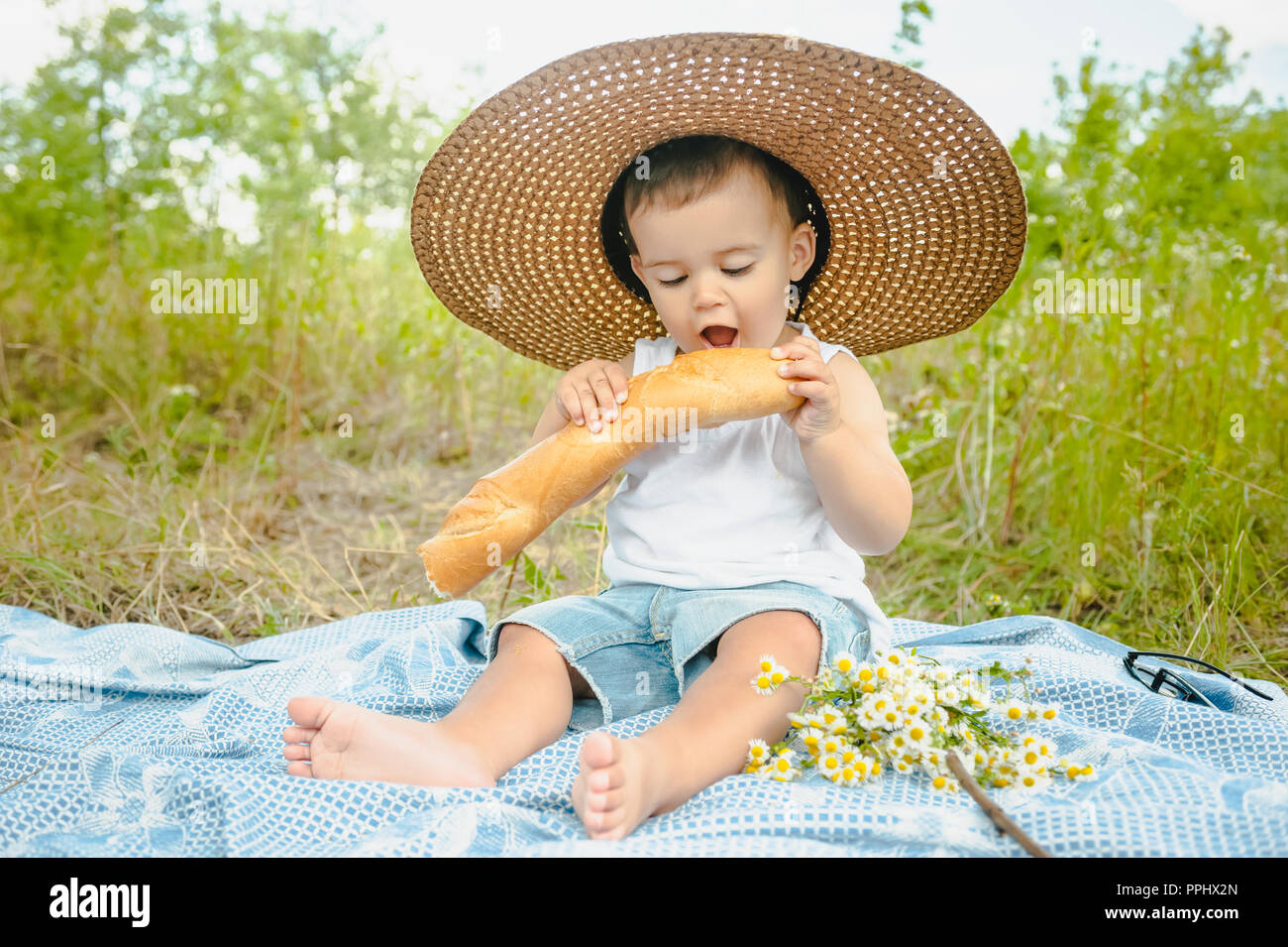 Adorabili toddler boy nel cappello di paglia seduti su una coperta a picnic  e mangiare la baguette Foto stock - Alamy
