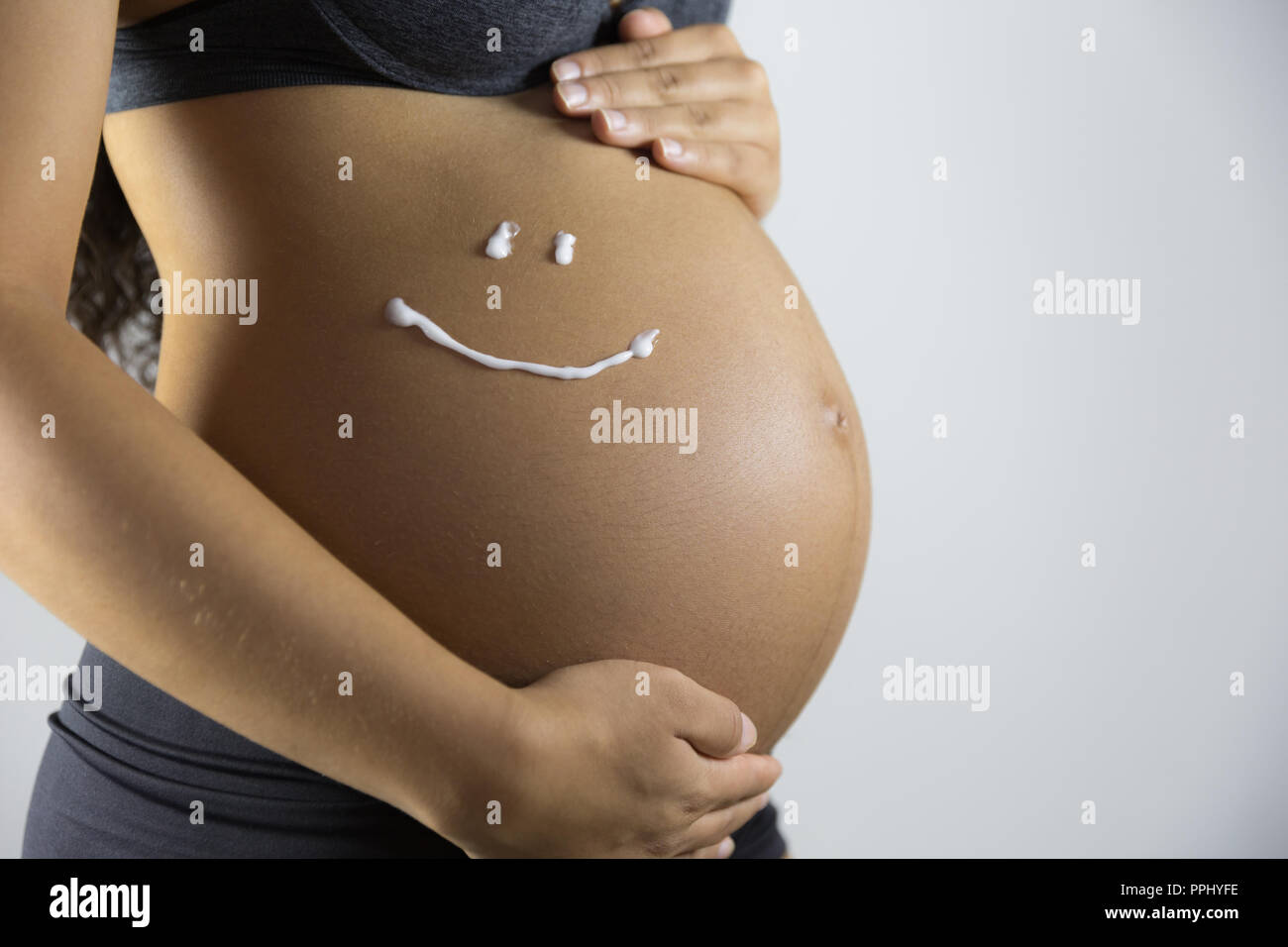 La gravidanza e la cura della pelle. Ventre della donna incinta e sorriso da crema idratante per le smagliature. Foto Stock