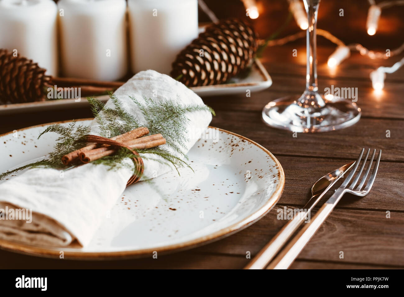 Ringraziamento impostazione tabella tra candele bianche e i coni. Piastra in ceramica con coltello e forchetta su un tovagliolo di lino. Il concetto di una cena di gala. Foto Stock