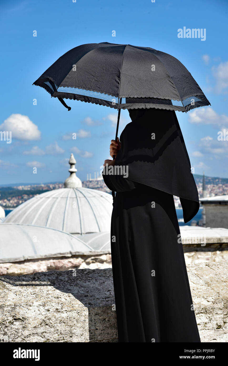 Signora in costumi islamici ripara dal calore del giorno sotto il suo ombrello presso la Moschea Süleymaniye, Istanbul, Turchia. Foto Stock