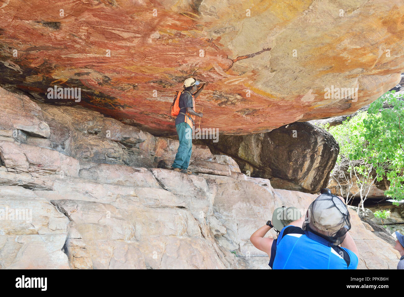 Guida aborigena sottolineando le opere in una roccia galleria d'arte sul colle Injalak di Arnhem Land, Territorio del Nord, l'Australia Foto Stock