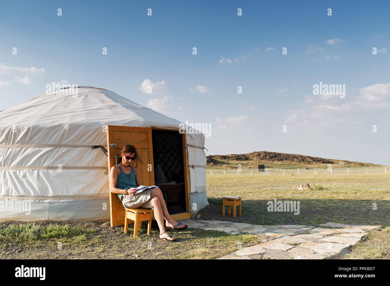 Una giovane donna è seduta davanti a un mongolo ger nel deserto di Gobi e sta leggendo un libro e Mongolia Foto Stock