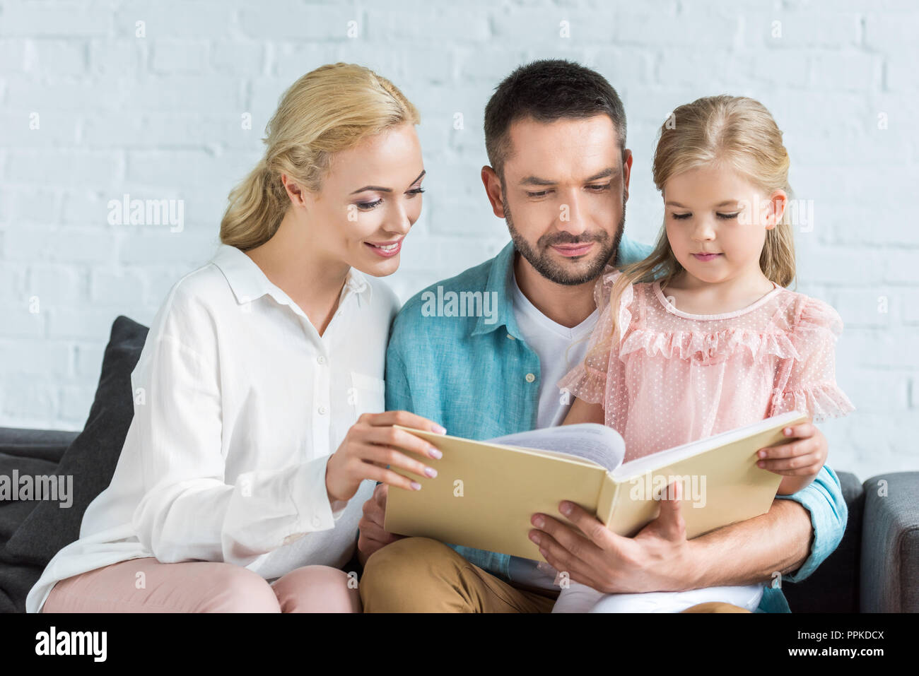 La famiglia felice con un bambino libro insieme a casa Foto Stock