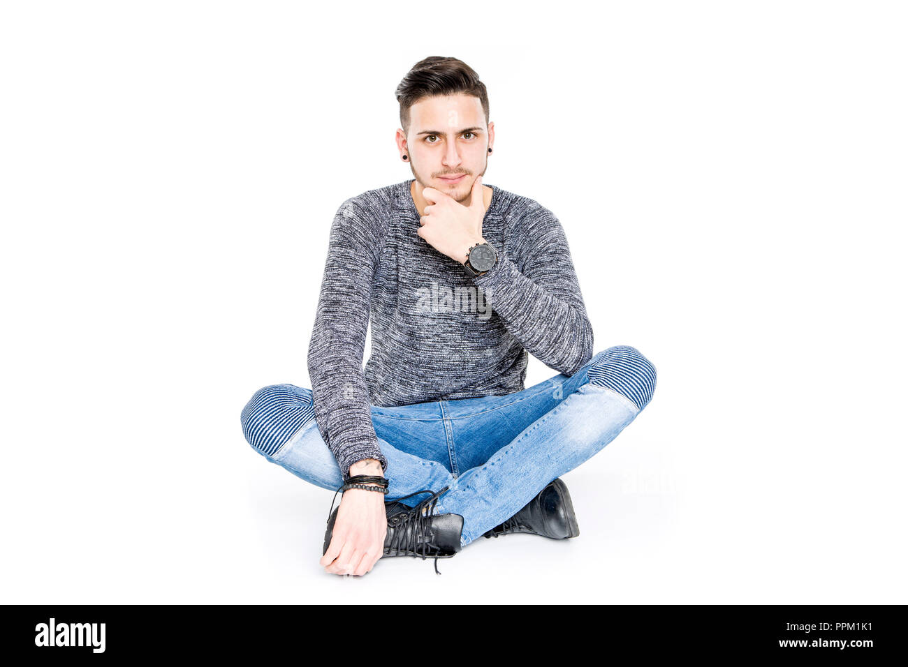 Casual bruna giovane uomo seduto sul pavimento ritratto sorridenti - isolato in uno sfondo bianco studio Foto Stock