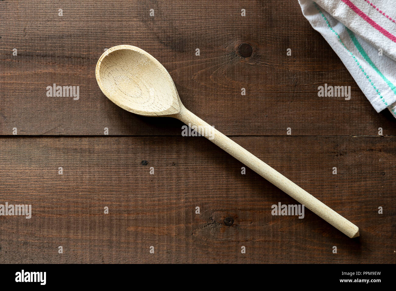 Cucchiaio di legno giacente su un panno assorbente. Su di un legno scuro dello sfondo. Foto Stock