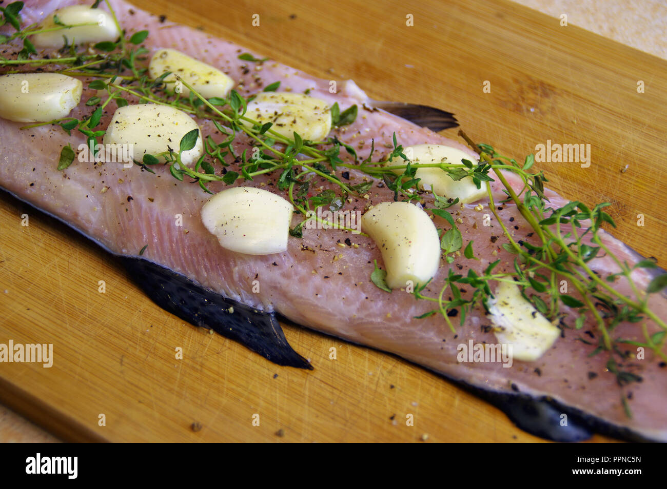 Crudo fresco di pesce preparati per la cottura. Filetto di trota con erbe aromatiche, aglio e spezie su una tavola di legno Foto Stock