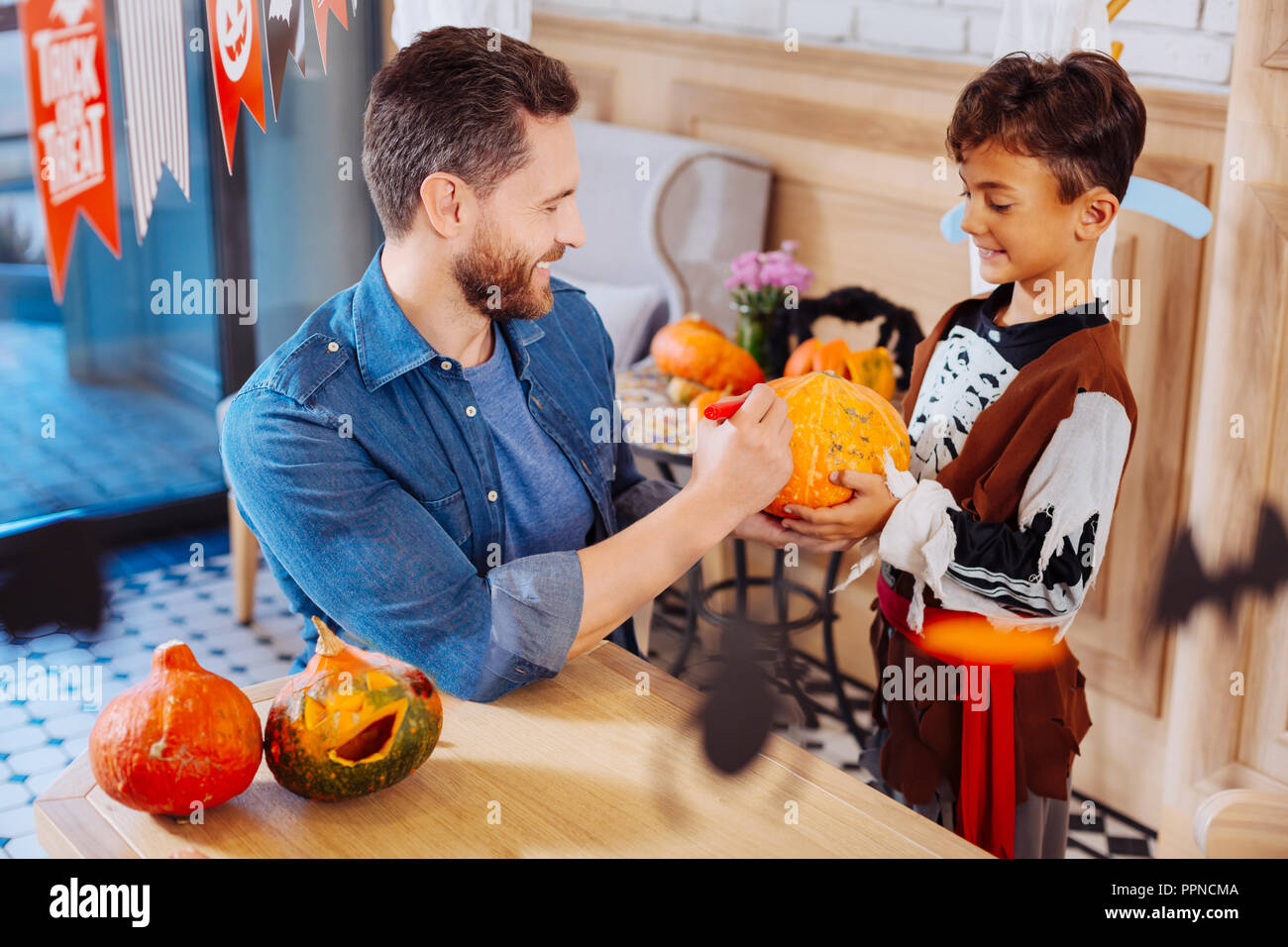 Padre sorridente indossando il denim shirt zucca di colorazione per la festa di Halloween con figlio Foto Stock