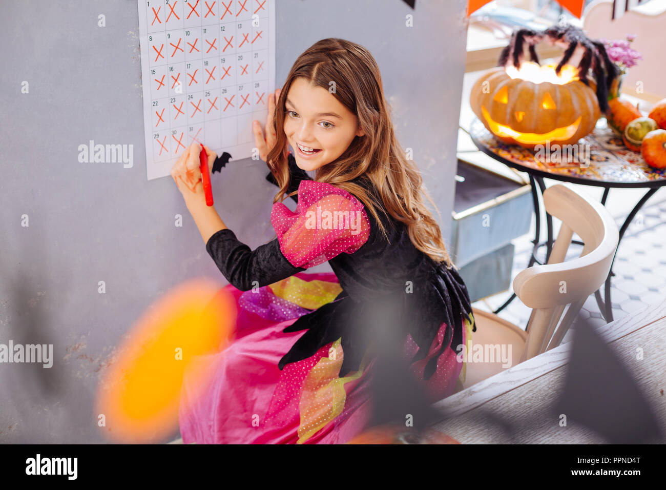 Divertenti ragazza alla moda indossando abiti di Halloween in piedi vicino al suo calendario da parete Foto Stock