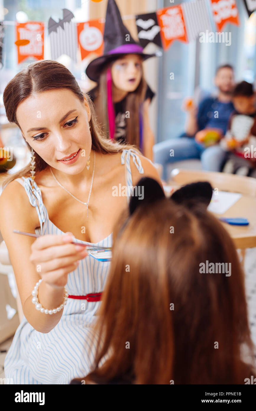 Dai capelli scuri che indossa insegnante bianca a strisce vestito dipinto volti di bambini Foto Stock