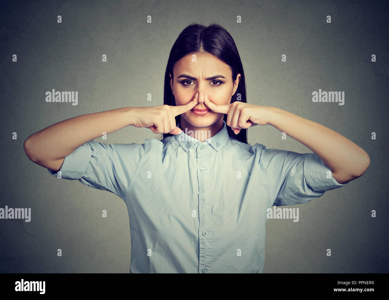 Donna pizzichi di naso con le dita guarda con disgusto puzza qualcosa di cattivo odore isolato su sfondo grigio. Foto Stock