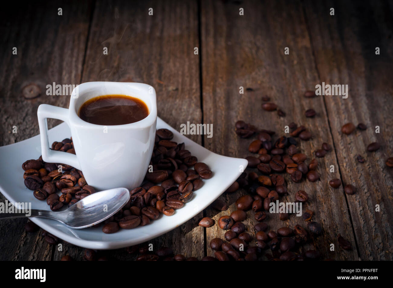 Un quadrato tazza di caffè sul vecchio tavolo in legno con fumo, alcuni grani un cucchiaio Foto Stock