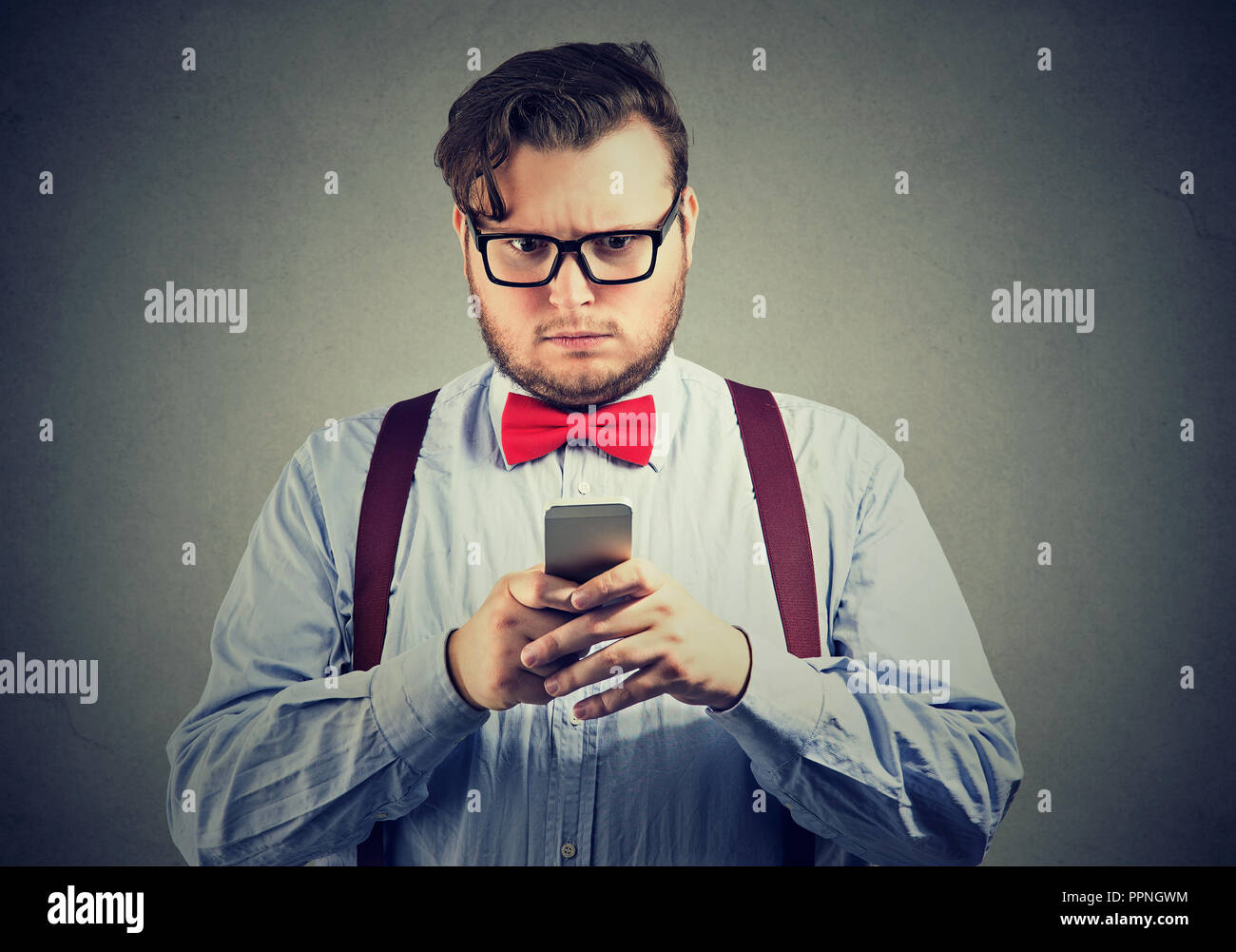 Confuso grave alla ricerca di uomo pensando cosa rispondere al messaggio di testo ricevuto sul telefono cellulare isolata sul muro grigio Sfondo. Espressione di faccia Foto Stock