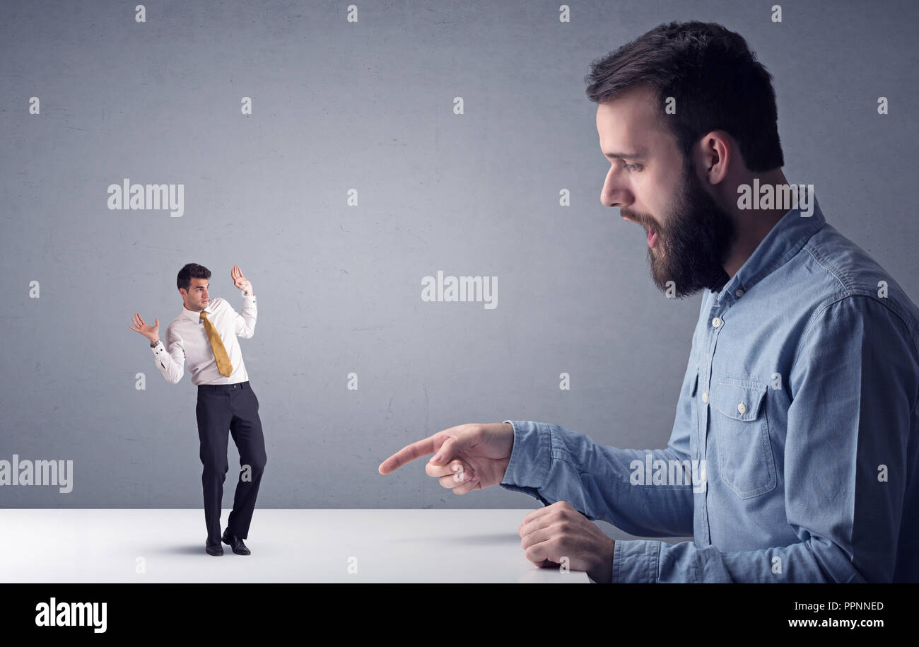 Giovane imprenditore professionale essendo arrabbiato con un altro imprenditore in miniatura di fronte a uno sfondo grigio Foto Stock