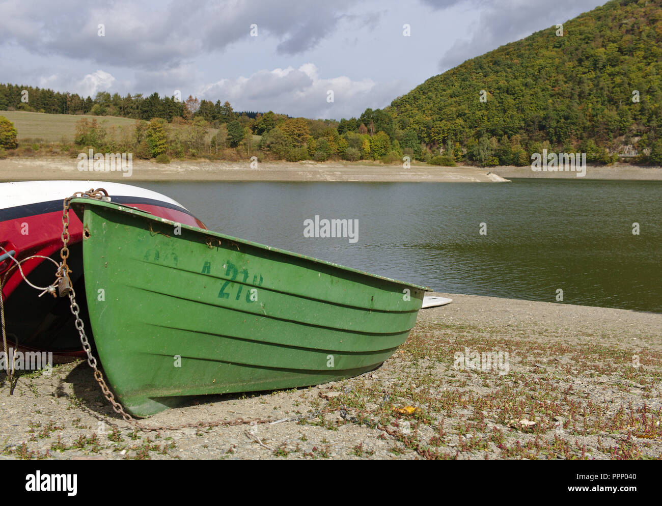 Diemelsee, Germania - riva del lago con spiaggia ghiaiosa, spiaggiata barca verdi e colline boscose della distanza Foto Stock