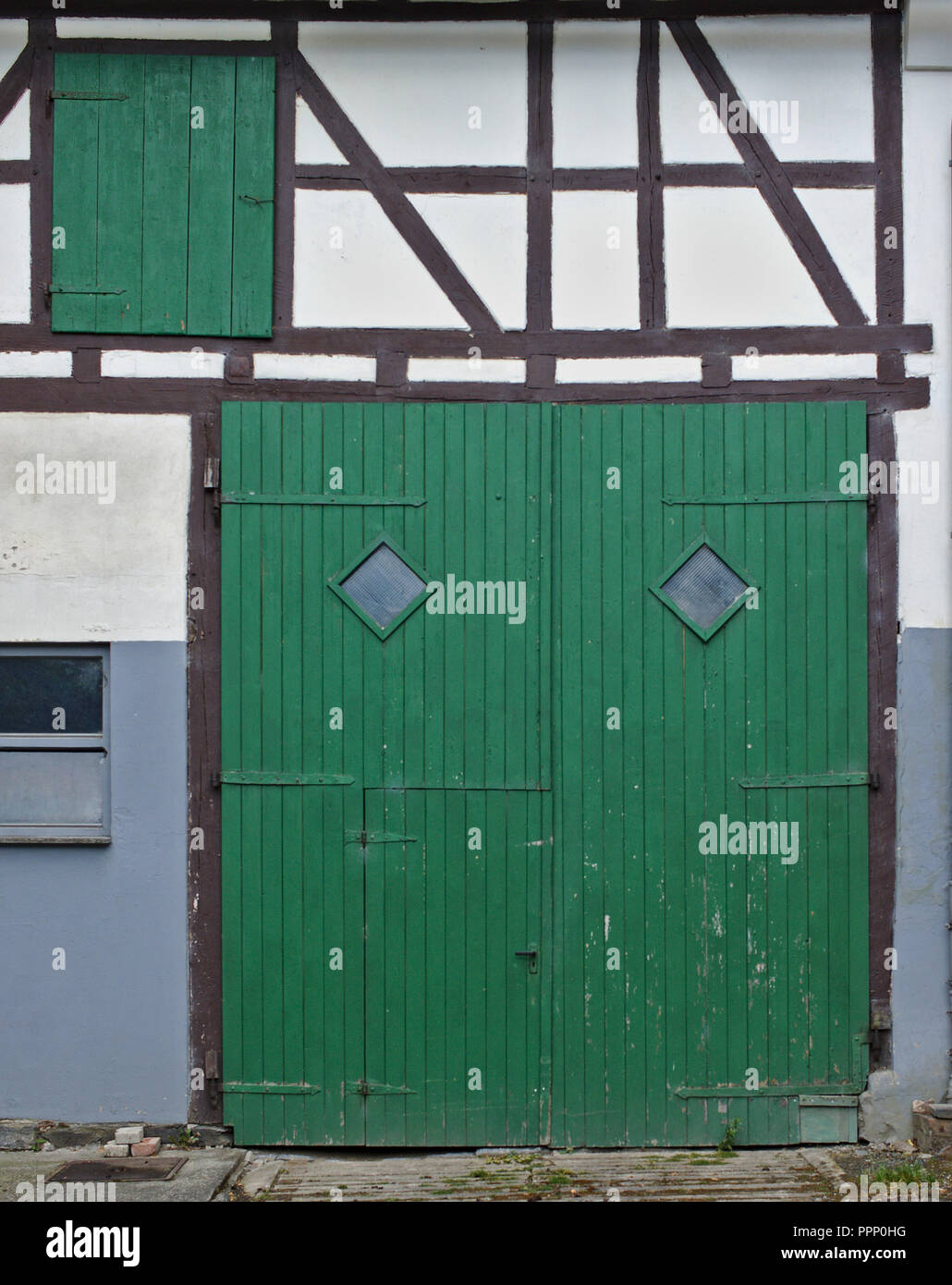 White a struttura mista in legno e muratura con parete verde grande fienile in legno porta e più piccolo di legno verde Porta in secondo piano Foto Stock