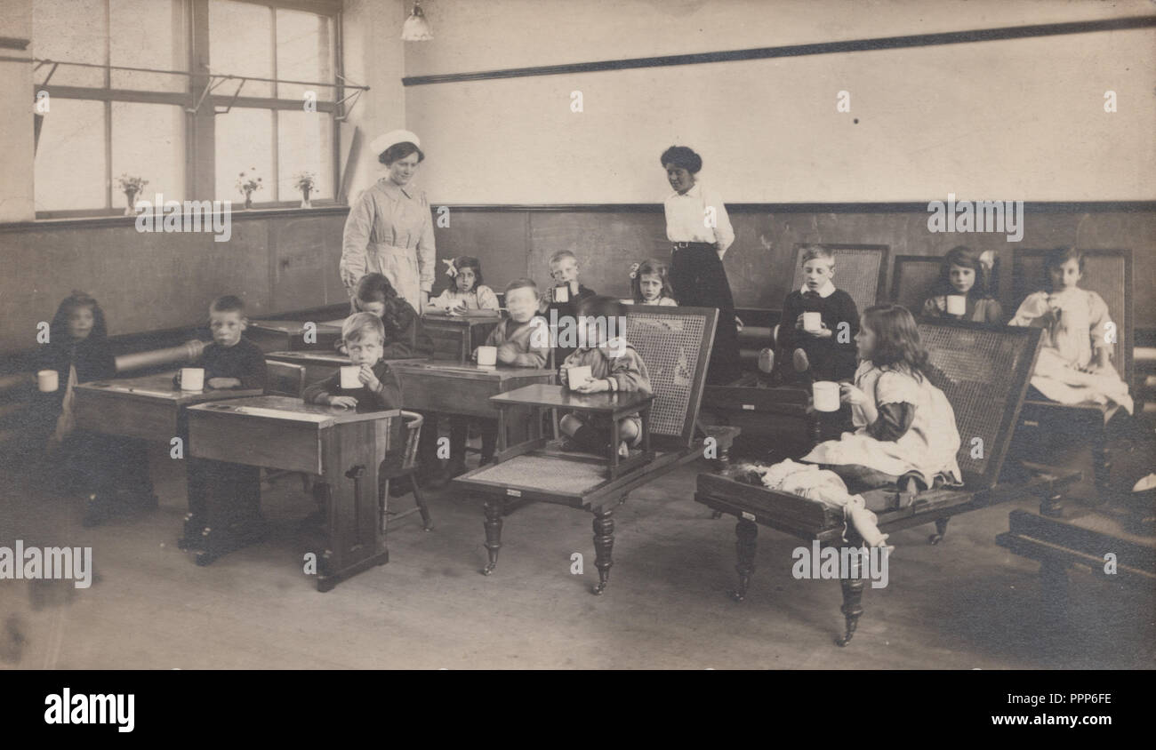 Vintage Edwardian fotografare dei bambini di bere in un aula scolastica. Insegnante e un infermiere presente. Foto Stock