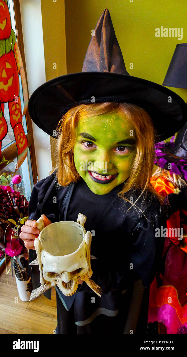 Ragazza bambino con una verde faccia a faccia la vernice, vestito in un kid Halloween costume strega, indossando un nero streghe e cappello abito nero. Foto Stock