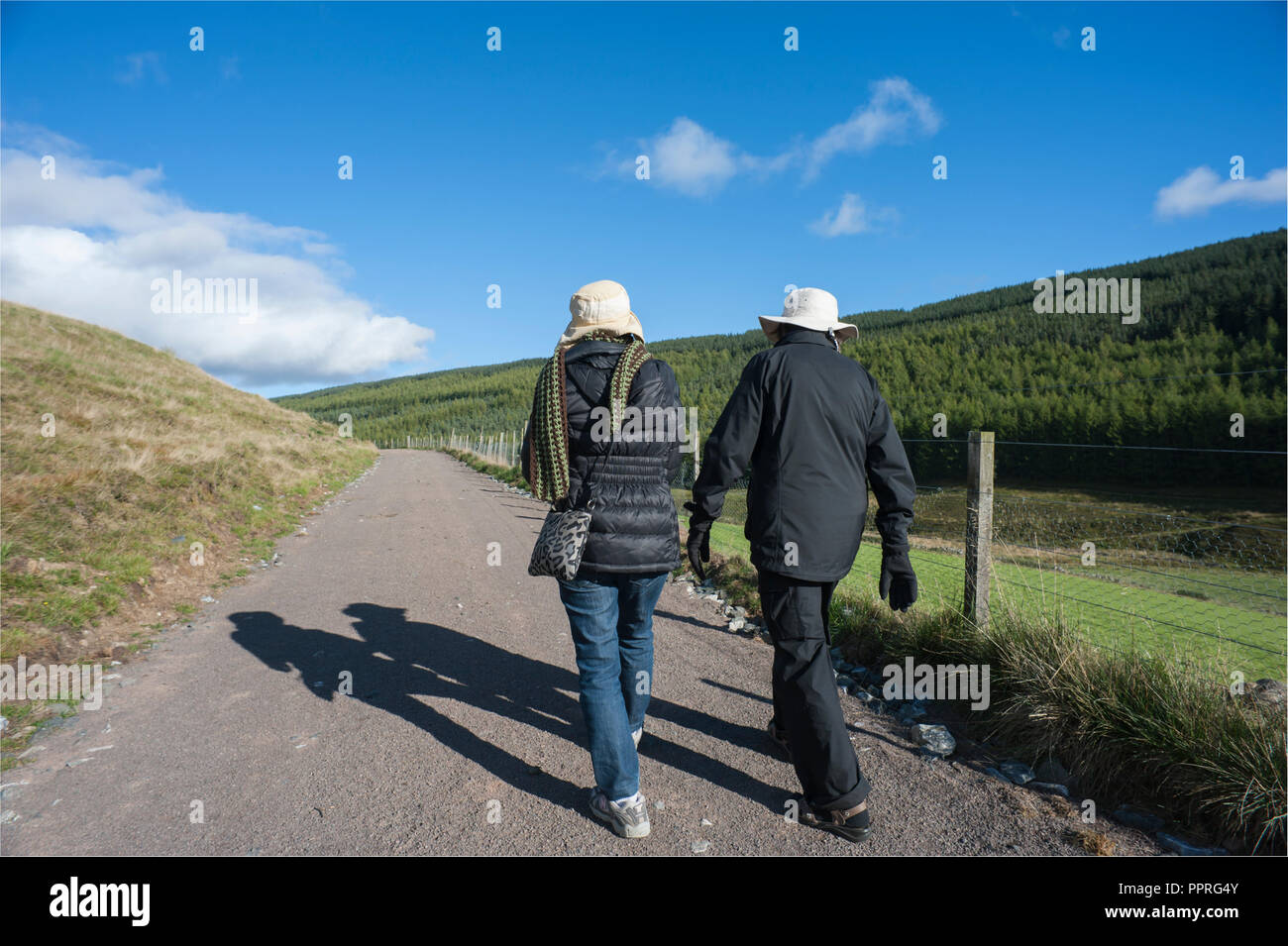 Vista posteriore o simili due femmine in nero giacche a vento e cappelli beige a camminare insieme sulla strada di fattoria in colline di Glen Isla Foto Stock