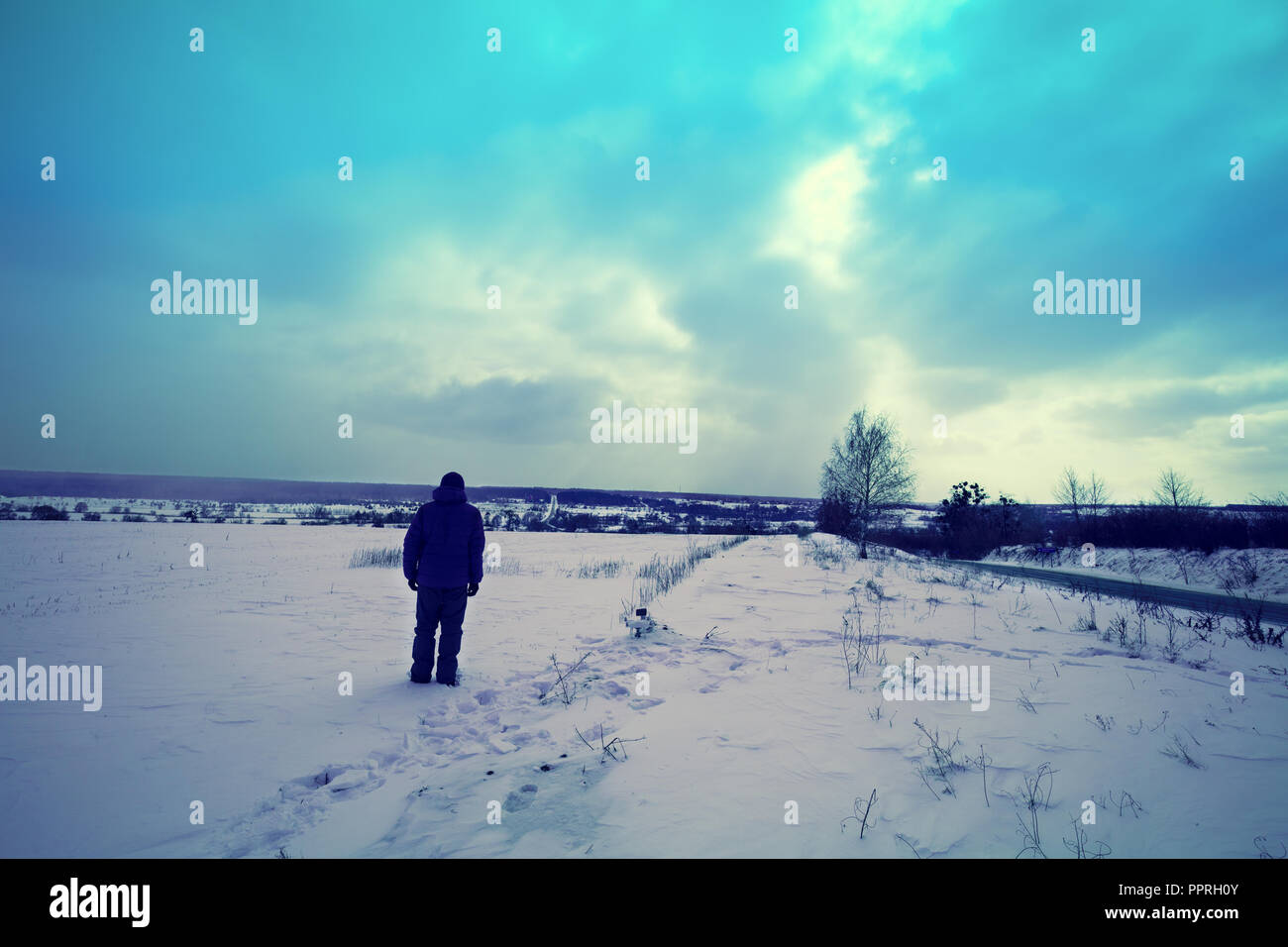 Silhouette di un uomo in piedi sul campo nevoso e guardando il drammatico cielo tempestoso Foto Stock