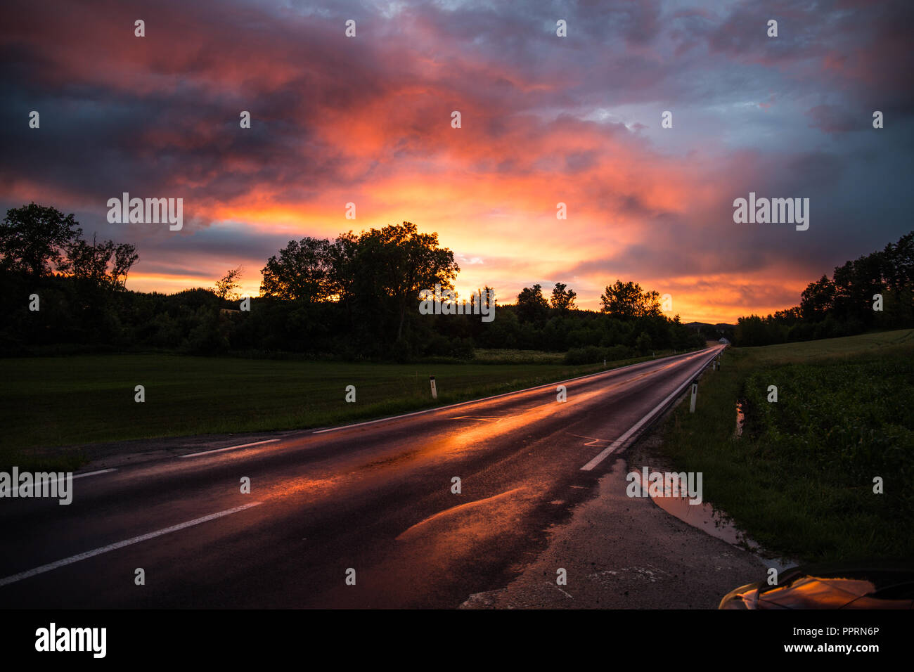 Una strada bagnata è che riflettono i colori del tramonto Foto Stock