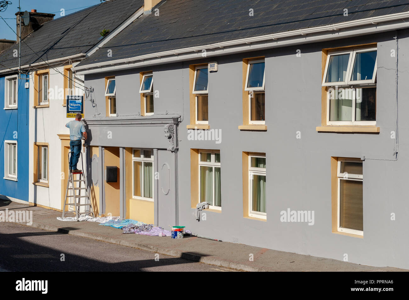 Un uomo su una scala a pioli verniciatura di una casa in Drimoleague, West Cork, Irlanda in una giornata di sole Foto Stock