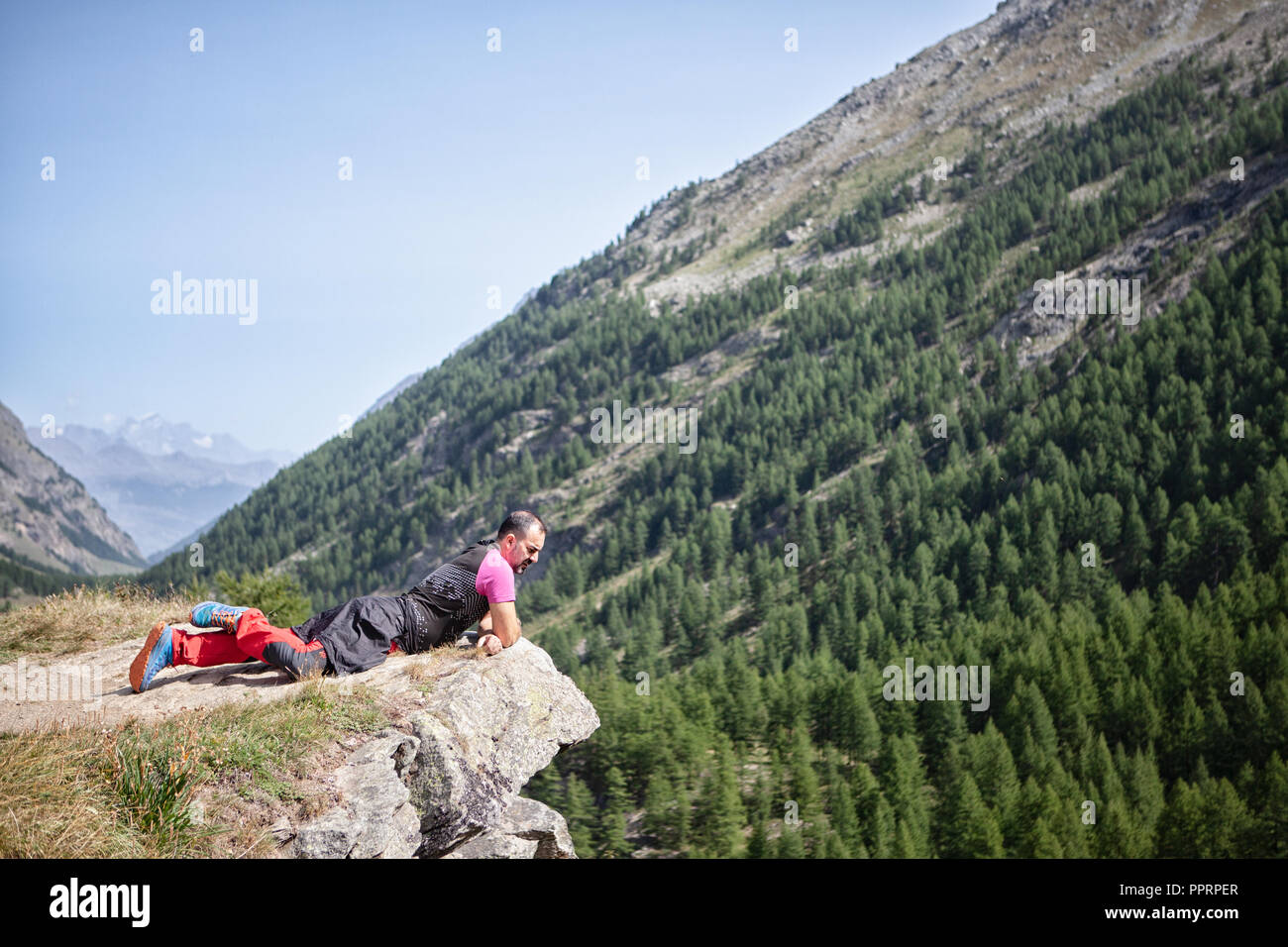 Uomo disteso sul precipizio guardando il paesaggio di montagna Foto Stock