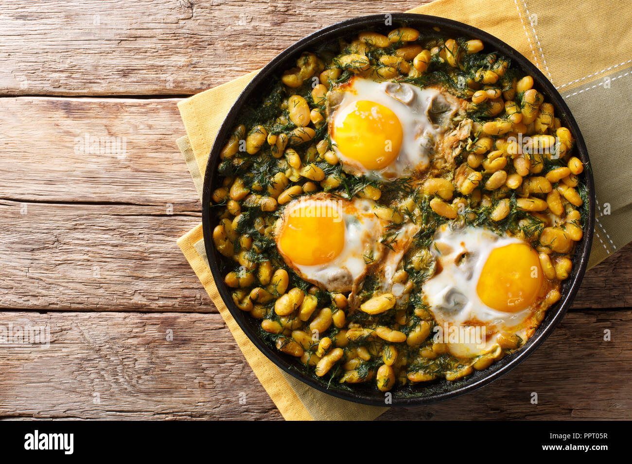 Gustoso piatto iraniano stufato di fagioli e aneto con uova fritte, aglio, curcuma close-up in una padella su una tavola orizzontale di vista in pianta da sopra Foto Stock