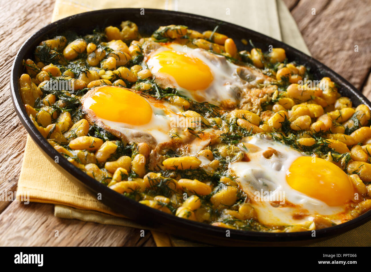 Gustoso piatto iraniano stufato di fagioli e aneto con uova fritte, aglio, curcuma close-up in una padella su una tavola orizzontale. Foto Stock