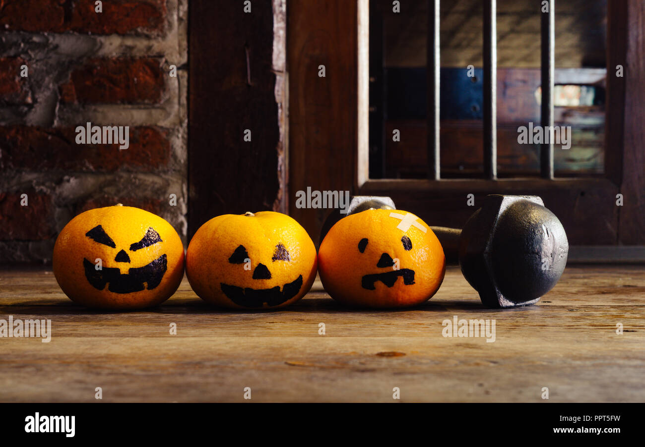 Tre arance con zucche di Halloween faccia con ferro nero dumbbell. Festa di Halloween con fitness, esercizio che lavora fuori, di peso e di dieta, healt Foto Stock