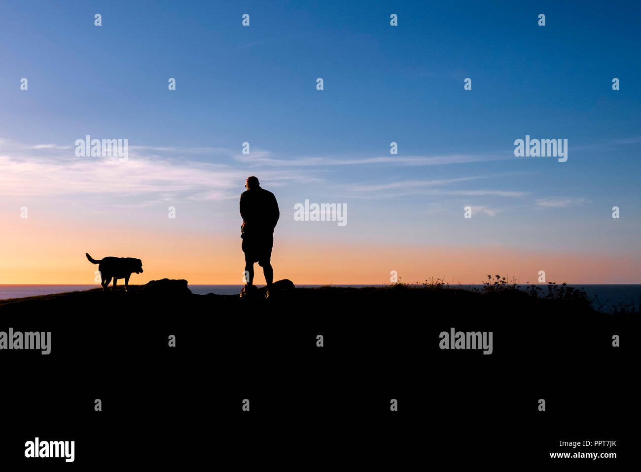 Un uomo e il suo cane visto in silhouette contro un tramonto a Newquay in Cornovaglia. Foto Stock
