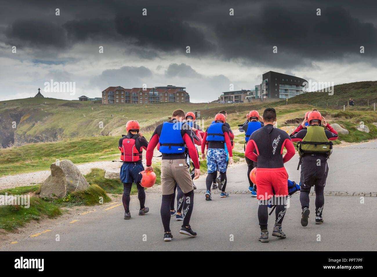 Un gruppo di persone a piedi lungo una strada per avviare una sessione di coasteering sulla costa di Newquay in Cornovaglia. Foto Stock