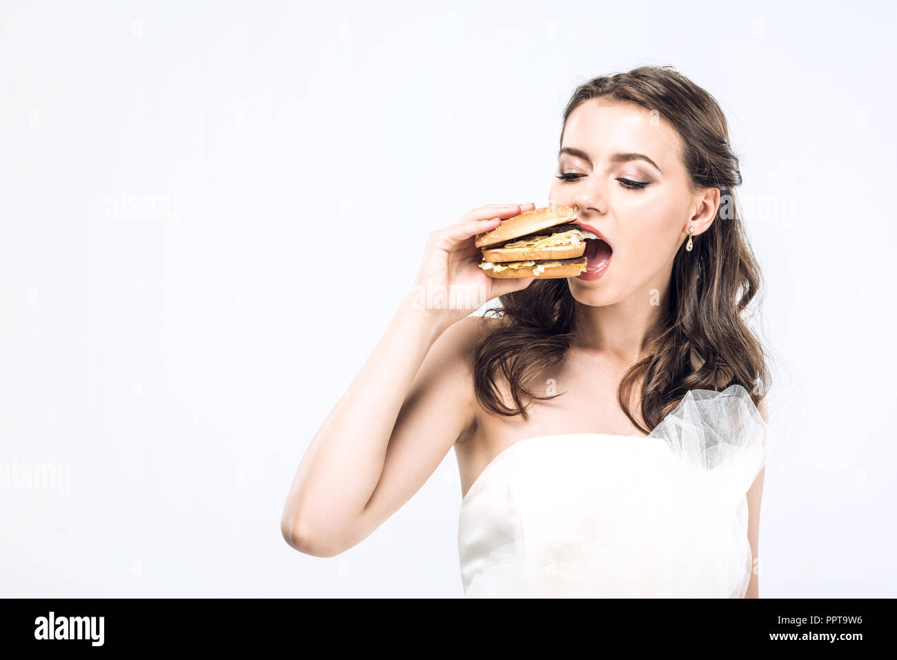 Fame giovane sposa in abito da sposa mangiare big burger isolato su bianco Foto Stock