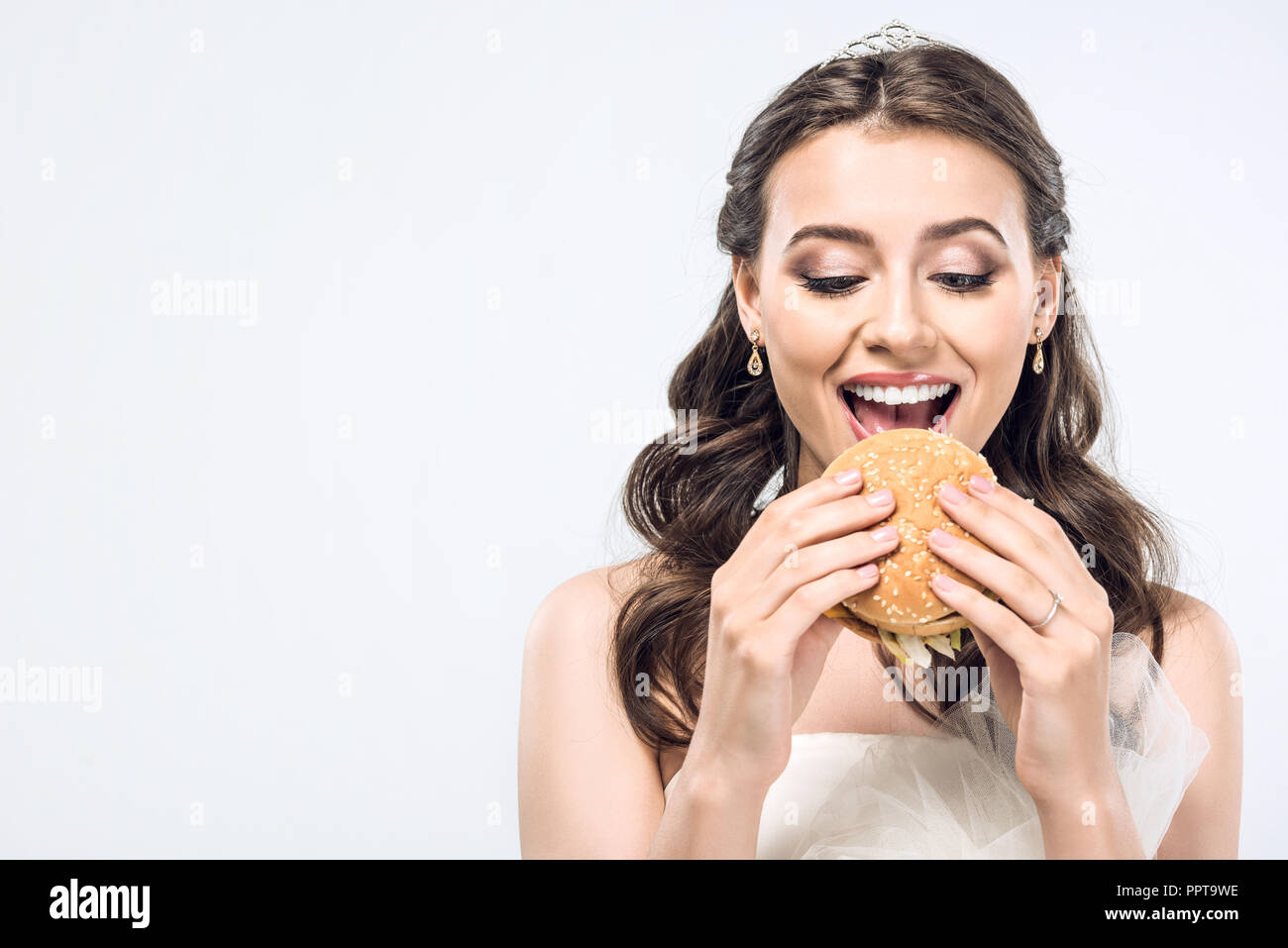 Felice giovane sposa in abito da sposa di mangiare hamburger isolato su bianco Foto Stock