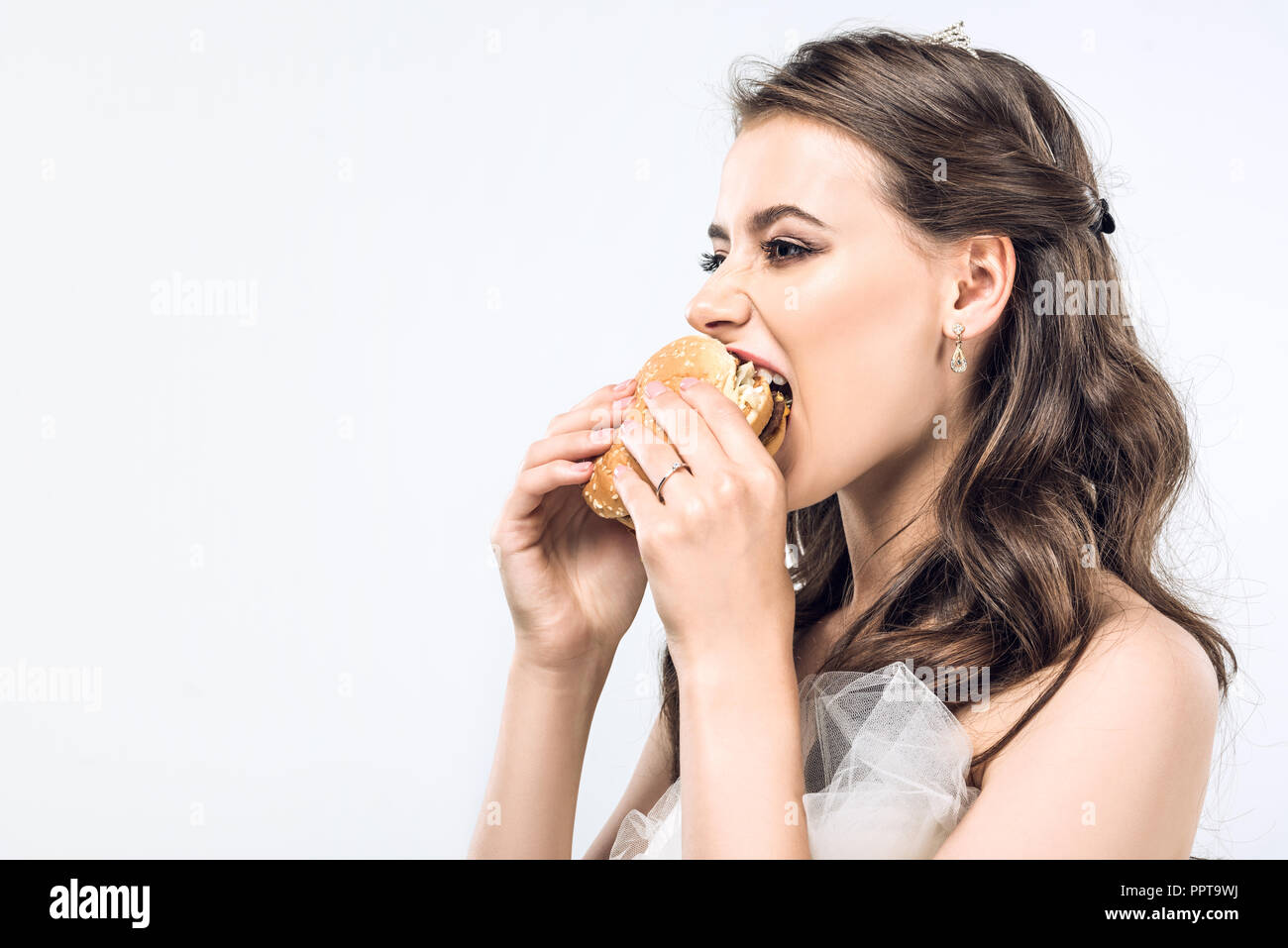 Close-up ritratto di fame giovane sposa in abito da sposa di mangiare hamburger isolato su bianco Foto Stock