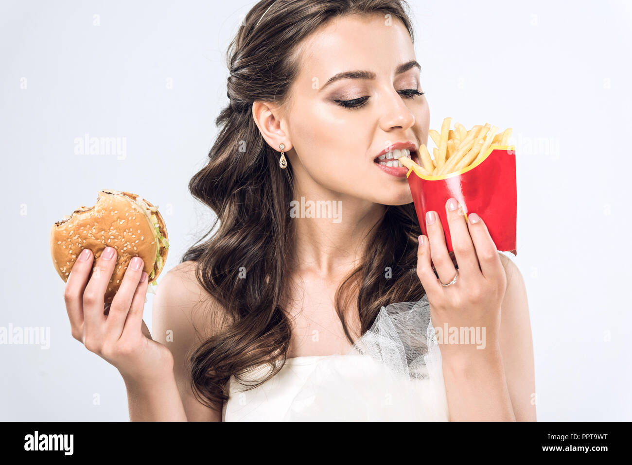 Giovane sposa in abito da sposa di mangiare hamburger e patatine fritte isolato su bianco Foto Stock