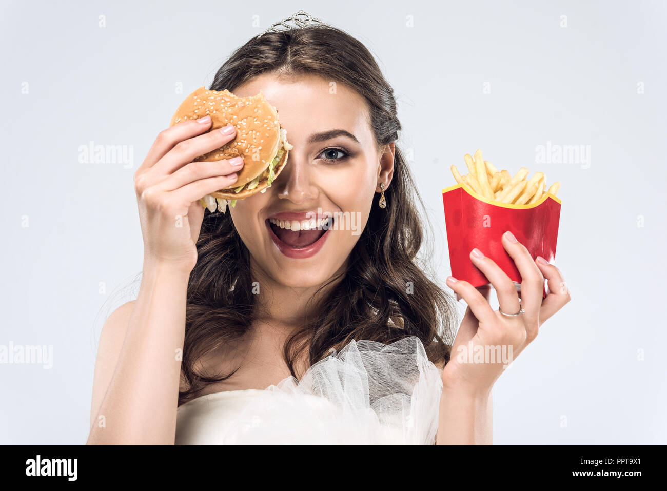 Felice giovane sposa in abito da sposa con hamburger e patatine fritte isolato su bianco Foto Stock