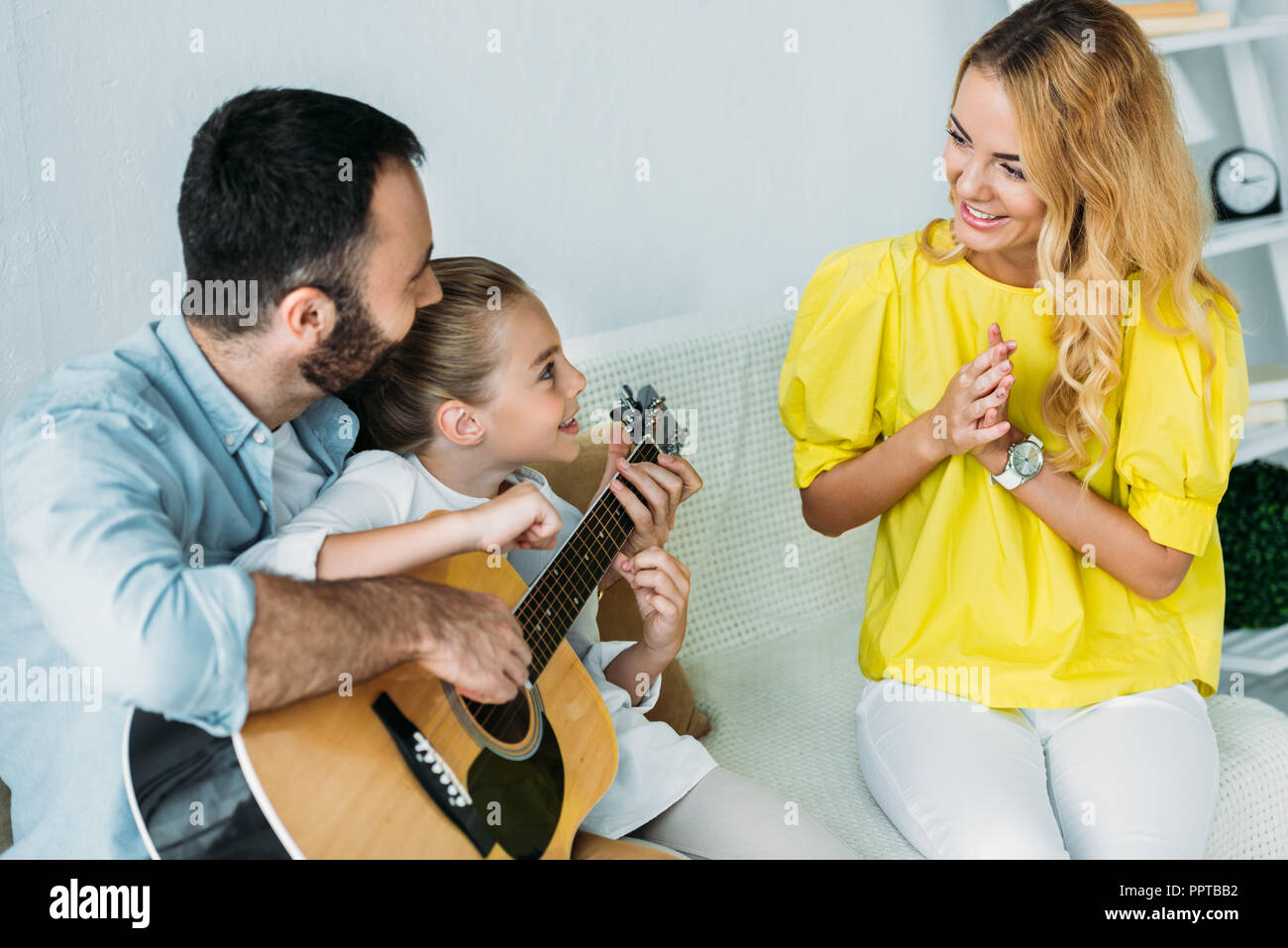Padre e figlia a suonare la chitarra per la madre a casa mentre lei battendo le mani Foto Stock
